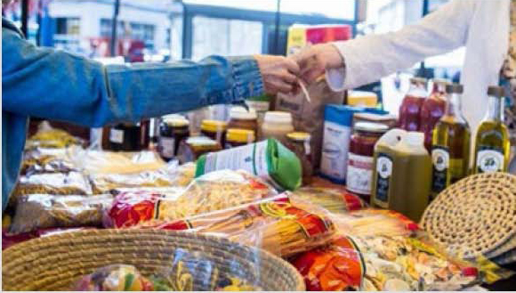 Una persona está comprando productos delante de un mostrador con mercadería de la economía social.