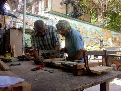 Dos personas están trabajando con maderas y herramientas en un patio al aire libre.